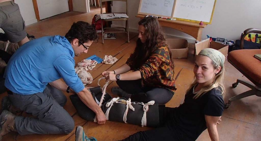 Two people work to brace the leg of another during wilderness first aid training 